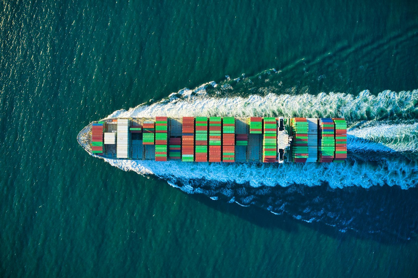 Container ship under way at sea seen from above, trailing a white wake